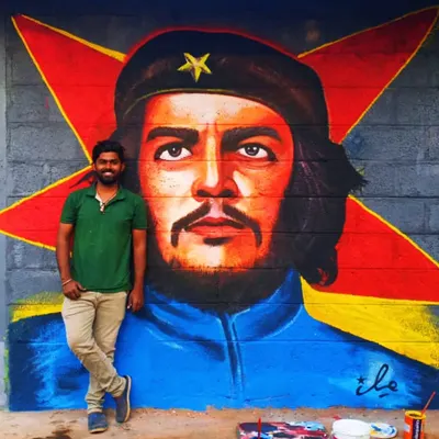 A finished portrait of Che Guevara, using bold colors and a starburst background to create a visually striking mural on an exterior wall.