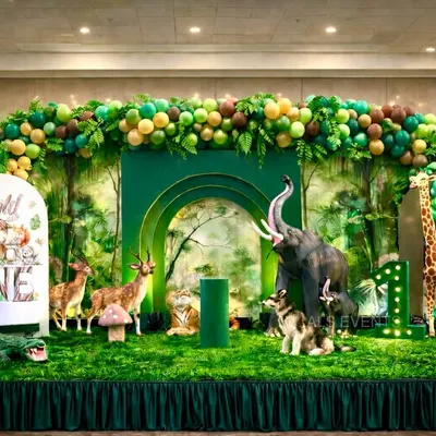 A wide view of our "Wild One" jungle stage. I use a mix of realistic animal props like an elephant, giraffe, and deer, along with a multi-layered green backdrop and a custom light-up number to create a stunning focal point.