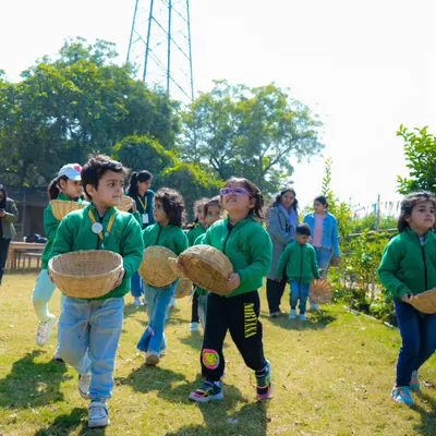 A group of young students in matching green jackets, excitedly carrying their baskets for a vegetable harvesting activity.