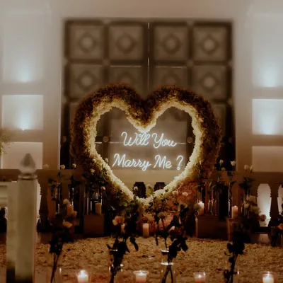 The perfect setup for a magical question. We capture all the beautiful details of your proposal decor, like this neon sign inside a heart of flowers, setting the stage for a resounding "Yes!".