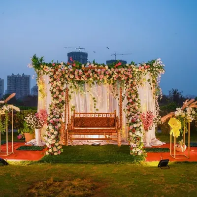 This wide shot shows the full sundowner setup against the evening sky. The floral arch and decorated swing create a central focal point, flanked by aesthetic floral stands, making it a grand and picturesque scene.