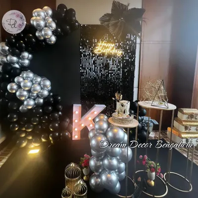 A sleek and stylish birthday setup in black and silver. The black sequin wall, 'Happy Birthday' neon sign, and metallic balloons create a glamorous and modern look.