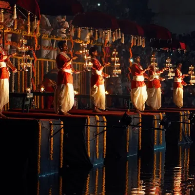 The serene Dev Deepawali Maha Aarti at Banganga Tank, with priests holding tiered lamps. The reflection in the water creates a truly magical, symmetrical scene.