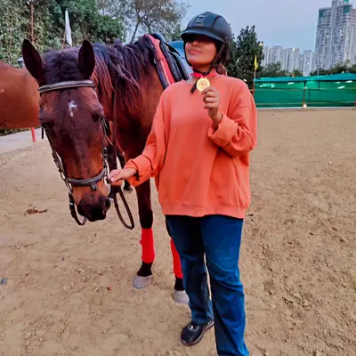 Celebrating a milestone! A student proudly shows off her medal after achieving a perfect canter, posing next to her trusted horse.