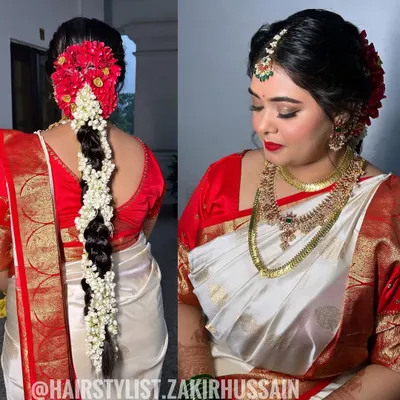 This is my signature South Indian bridal hairstyle. I created a traditional thick braid and meticulously adorned it with fragrant jasmine and vibrant red flowers, crafting a classic and timeless look for the main wedding ceremony.
