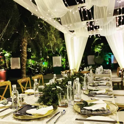 An intimate sit-down dinner setup in the courtyard of the Pullman New Delhi. The decor features a canopy of white drapes and fairy lights, creating a magical, starlit ambiance for a special evening.