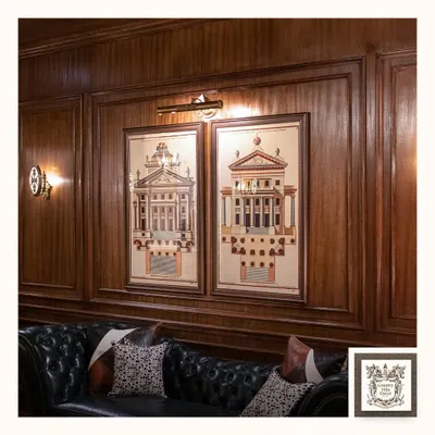 In this wood-paneled study, a classic picture light casts a warm, even glow over architectural prints, while a vintage-style wall sconce adds ambient light. This combination creates a sophisticated, layered lighting scheme.