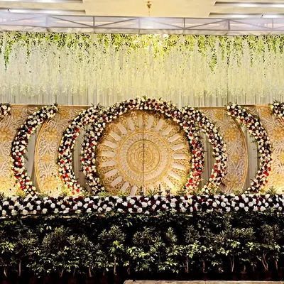 This is one of my most elaborate stage designs, featuring large carved panels in a gold and white theme. The multiple floral arches and dense greenery at the base give it a very grand and royal look, perfect for a large reception.