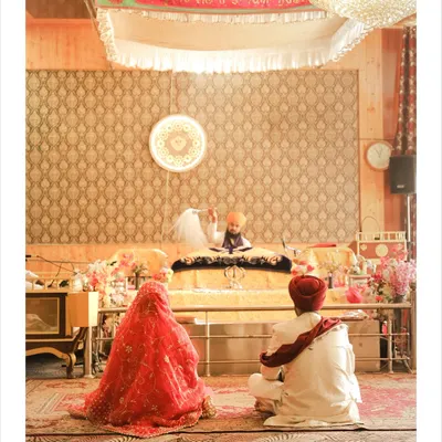 A wide shot of the Anand Karaj ceremony inside the Gurudwara. The couple is seen seated before the Guru Granth Sahib, capturing the spiritual essence of a Sikh wedding.