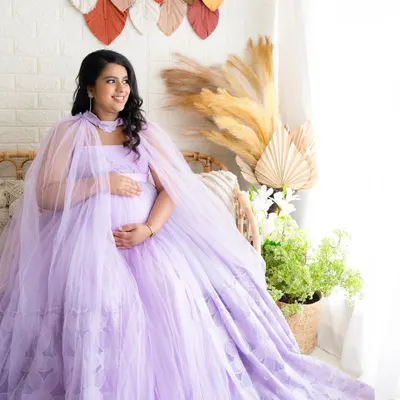A radiant solo portrait of a mom-to-be in a flowing lavender gown, seated in a boho-chic studio setup with pampas grass.
