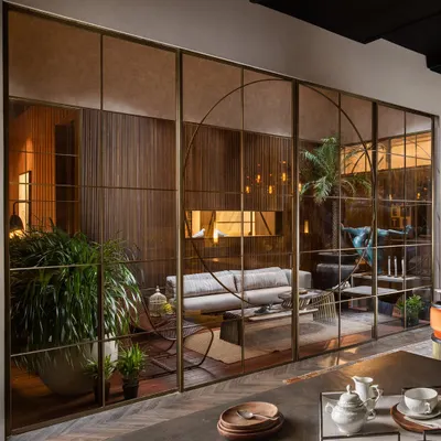 This floor-to-ceiling glass partition, encased in fine metal profiles, elegantly divides the living and dining areas. The design maintains an open, airy feel while creating distinct zones, with sliding doors for seamless movement between them.