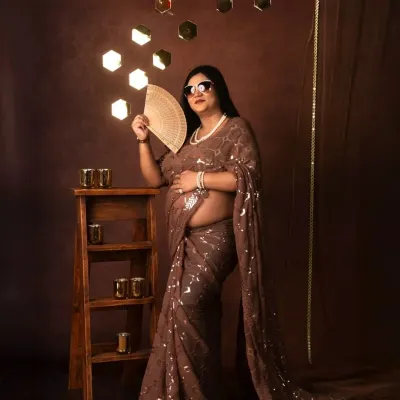 A glamorous and modern take on tradition. This mom-to-be shines in a sequined saree in our 'Shining Diva' setup, complete with stylish sunglasses and a fan.