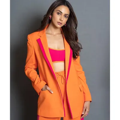 A full-length view of the vibrant orange and pink pantsuit from Antithesis. The wide-leg trousers and bold color blocking make it a modern power suit.