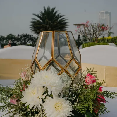 This centerpiece combines a modern gold-trimmed geometric lantern with a lush base of white chrysanthemums and pink roses. It's a perfect example of a small detail that adds a touch of warmth and sophistication to guest tables.