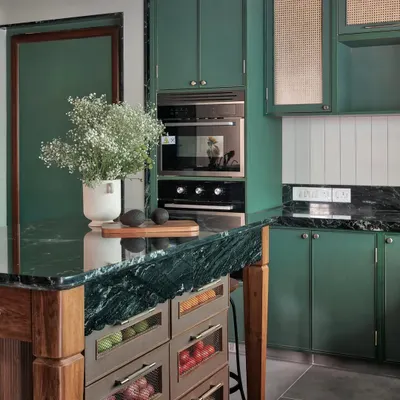 This kitchen is a study in rich, layered textures. The deep green of the cabinetry is balanced by the natural grain of the wooden island and the cool, veined marble countertop, creating a space that feels both grounded and full of character.