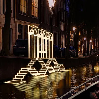 A close-up of the "Echoes of the Deep" light installation in Amsterdam. The glowing lines form an abstract representation of an Indian step-well, creating a piece of architecture made purely of light that interacts with its reflection in the canal water.
