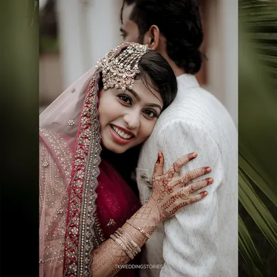 A warm and joyful portrait of a Muslim bride in a stunning red and gold outfit, embracing her groom. Her happy smile and the intricate henna are beautifully captured.