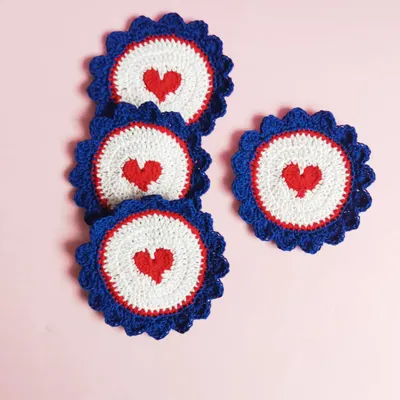 A set of our heart-themed crochet coasters. The design features a small red heart at the center of a white and blue scalloped circle, perfect for adding a little love to your coffee break.