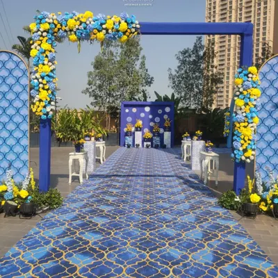 A grand entrance for a Haldi ceremony, featuring a bold blue archway adorned with yellow and blue flowers, leading down a patterned carpet.