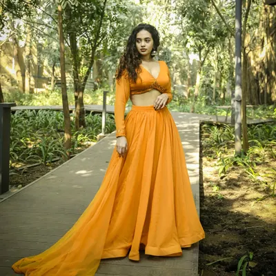 A beautiful portrait from an outdoor ethnic wear shoot. The natural green backdrop makes the vibrant orange lehenga pop, creating a fresh and elegant look perfect for a pre-wedding session.
