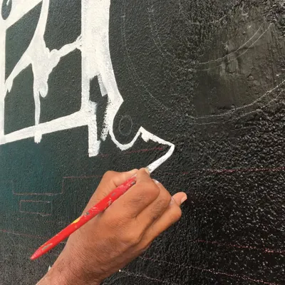A close-up of our artist's hand, carefully painting a crisp white line on a black textured wall. This level of detail and control is what defines our custom mural work.