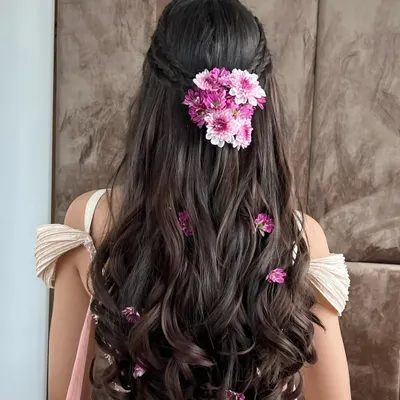 A beautiful half-up floral hairstyle perfect for a Mehendi or Haldi. The fresh pink daisies are woven through the hair for a soft, romantic look that complements the outfit.