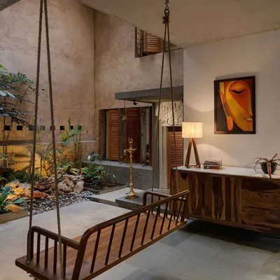 An indoor wooden swing offers a relaxing spot overlooking a tranquil, plant-filled courtyard. This traditional element is integrated into a modern context, providing a playful and nostalgic feature within the living space.