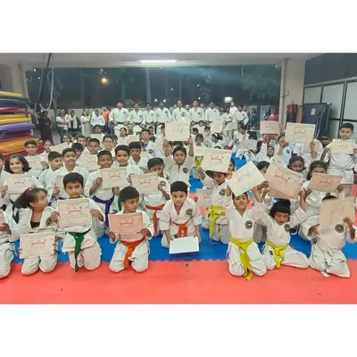 A hall full of smiling students holding their new certificates after a successful belt grading exam. This is a proud day for them and their parents.