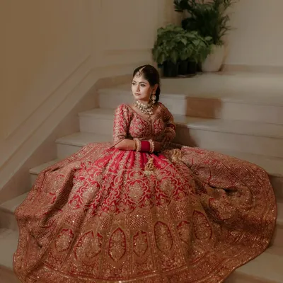 A breathtaking portrait of the bride seated on a grand staircase, her magnificent red and gold lehenga spread out around her. This shot is all about royal elegance and capturing the bride in her full splendor.