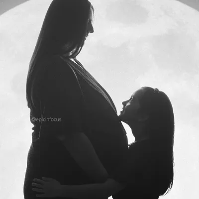 A touching and artistic silhouette of an older sister looking up at her mother's baby bump, a beautiful way to include a sibling in the maternity shoot.