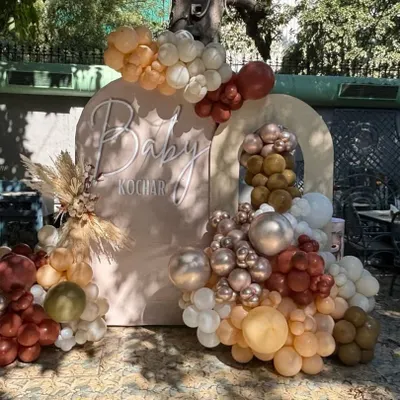 A chic boho-style baby shower backdrop with earthy-toned balloons, pampas grass, and a personalized "Baby Kochar" sign.