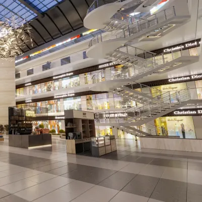This mall interior features a multi-level open atrium with a dramatic floating staircase, creating clear sightlines to the storefronts on each floor. The design encourages vertical exploration.