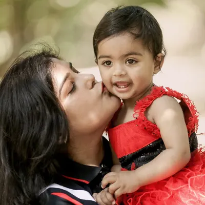 The pure joy of a mother's kiss. This candid outdoor shot captures a beautiful, unposed moment of affection between a mother and her smiling baby.