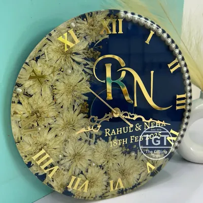 This is a 12-inch personalized resin clock I made for a couple. Their varmala flowers are set in a crescent moon shape against a shimmery royal blue base, with their monogram, names, and wedding date in gold.