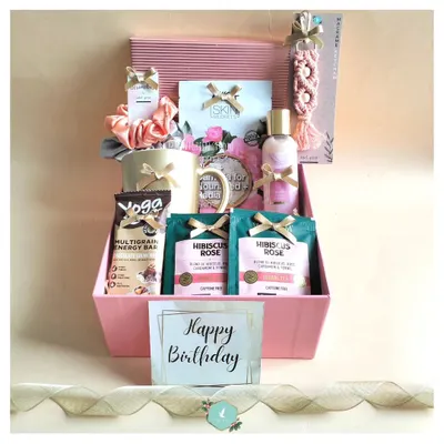 A birthday hamper designed to pamper. This pink-themed box includes hibiscus rose tea, a multigrain energy bar, a face mask, a personalized mug, and other self-care goodies.