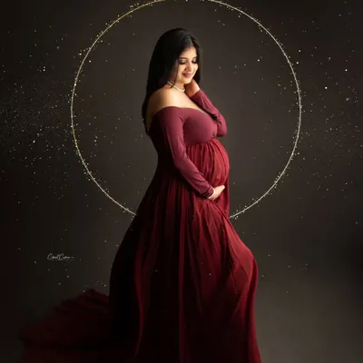 A magical and elegant portrait. The mom-to-be is framed by a glowing halo, her deep red gown and the sparkling lights creating a celestial feel.