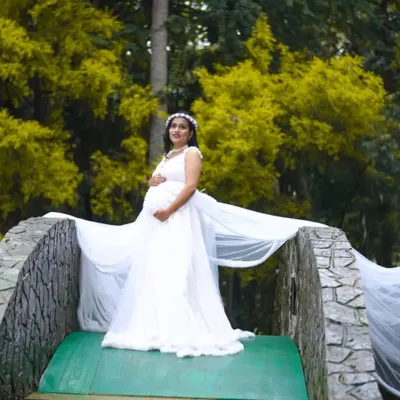 An expecting mother looking serene on a bridge, wearing my flowing white maternity gown. The long trail adds a touch of drama to this beautiful outdoor nature shot.