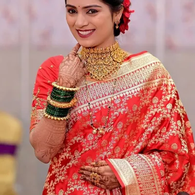 A happy bride in a red saree wearing a traditional gold-look choker, a classic choice for Maharashtrian and South Indian weddings.