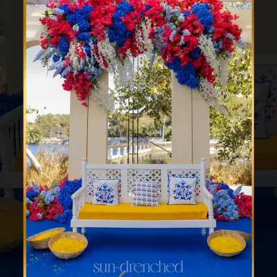 For this Haldi in Udaipur, we created a sun-drenched dream with a Caribbean-inspired theme. The seating for the couple was set against a backdrop of bold red, blue, and white flowers, overlooking the lake.