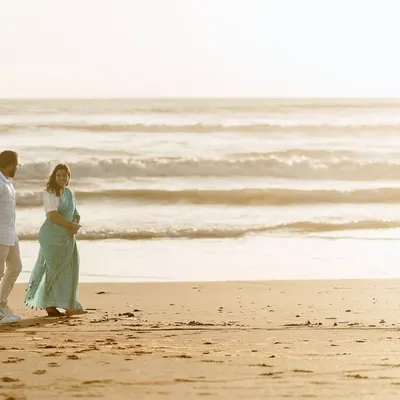 A wide-angle shot of a couple on a serene beach during the golden hour, capturing the vastness of the ocean and the intimacy of the moment.