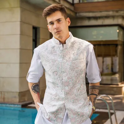 This sleeveless vest, with its delicate pastel floral embroidery, is a perfect example of effortless style. Paired with a simple white kurta, it's an ideal outfit for a daytime festive event or a Haldi ceremony.