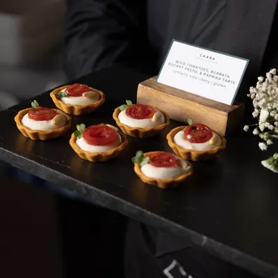 Wild tomato, burrata, and pesto tartlets, a perfect bite-sized appetizer. These gluten-free tarts are a crowd favorite, combining the freshness of cherry tomatoes with creamy burrata and our farm-fresh basil pesto.