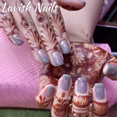 A set of square-shaped nails with a shimmering, color-shifting glitter polish that contrasts beautifully against intricate bridal mehendi designs.