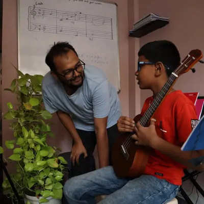 A perfect moment of mentorship. Our instructor guides a young ukulele student, with music theory visible on the whiteboard behind them.
