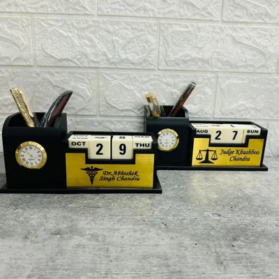 This image shows two of my lifetime calendar desk organizers side-by-side. They feature a perpetual block calendar, an analog clock, and pen holders, customized here for a doctor and a judge with their names and professional symbols.