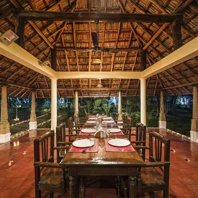 Our open-air restaurant set for dinner. The traditional thatched roof and wooden furniture create a natural and calming atmosphere to enjoy your wholesome Ayurvedic meals.