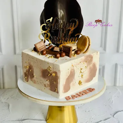 A chic and modern square birthday cake. This design features a marbled chocolate and vanilla frosting, a glossy chocolate sail, macarons, and a sprinkle of gold leaf for an elegant finish.