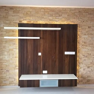 A custom TV unit featuring a dark wood back panel set against a stone-cladding wall. The floating white shelves and console create a modern, airy feel with integrated backlighting.