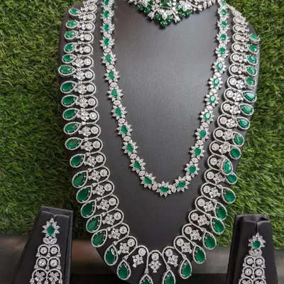 This is the ultimate reception look! A grand two-layered American Diamond haaram with emerald stones, paired with a matching choker and earrings. This set is designed to make you feel like a star on your big day.