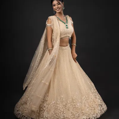 A joyful, full-length shot of a model in a stunning cream and gold lehenga, complete with an emerald jewellery set. This captures the grandeur of modern Indian bridal fashion.